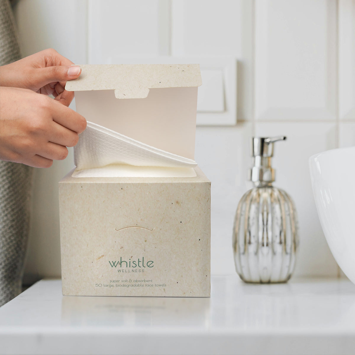 Taking a fresh Whistle XL face towel from its resealable box beside a bathroom sink